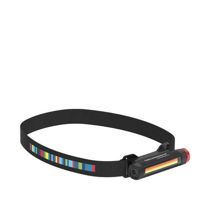 Digital photograph of a Scangrip black headlamp featuring a multi-colored striped band, a black rectangular light unit labeled "COLOUR MATCH", and an orange-yellow gradient light bar with a red cap
