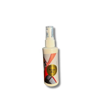 White spray bottle with a clear cap featuring an abstract label with red and black geometric shapes and a prominent gold seal marked Revision #5