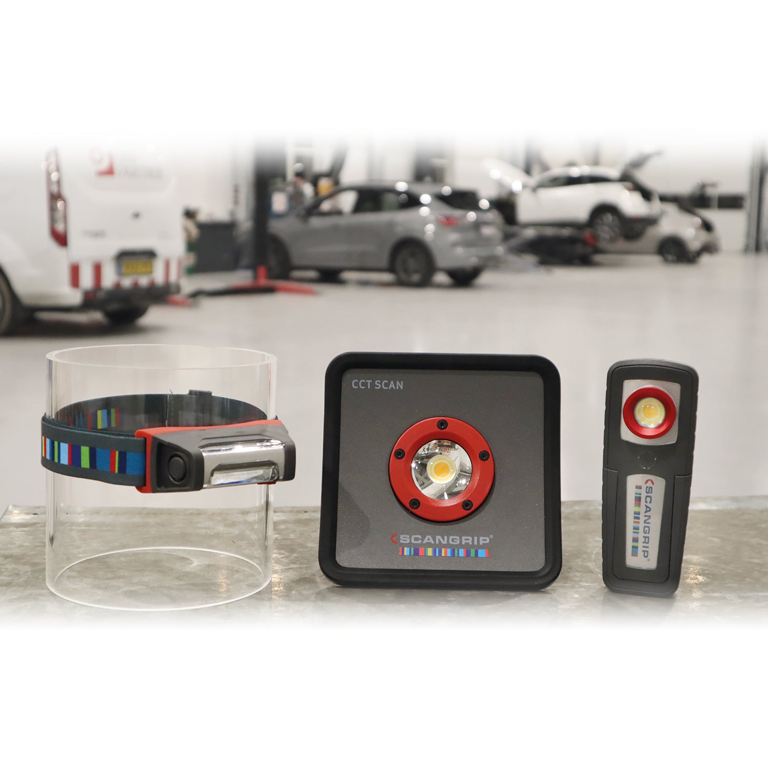 Three Scangrip professional LED work lights, including a headlamp with a colorful striped strap, a square CCT SCAN light with a red ring, and a rectangular inspection light, displayed in a blurred car workshop background with vehicles on lifts