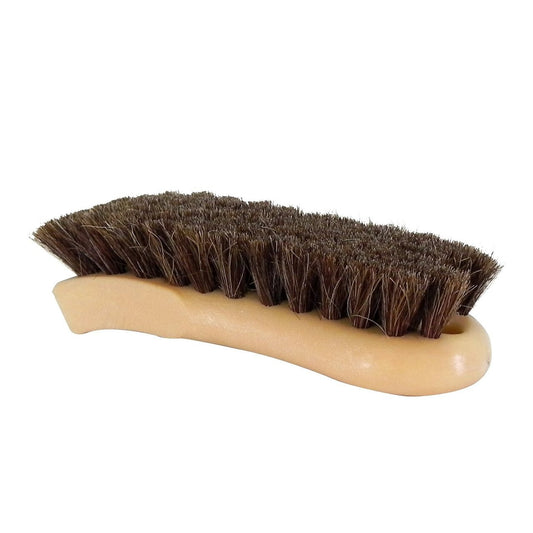 A shoe brush with a light tan ergonomic curved plastic handle and dense dark brown natural bristles