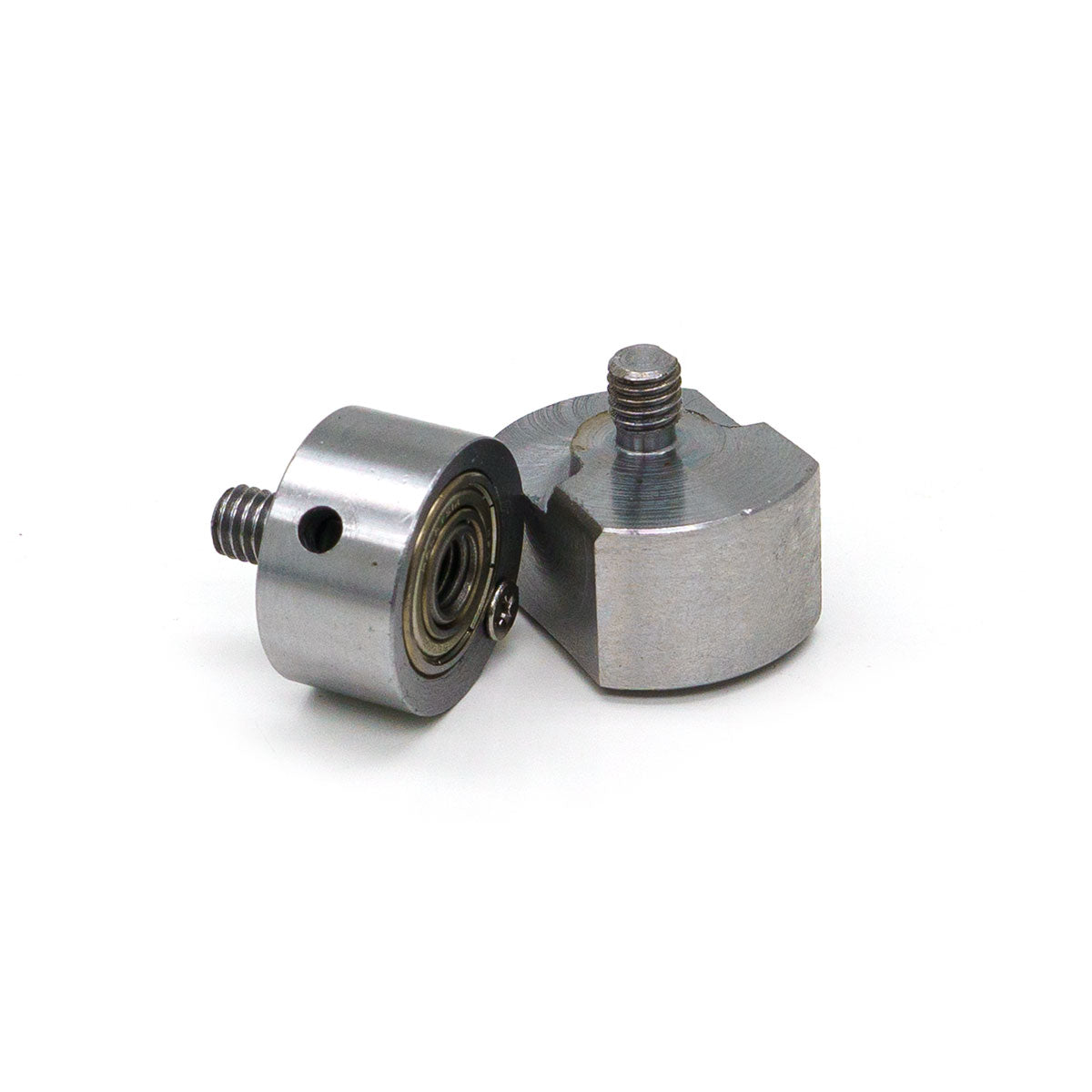 Two brushed silver-grey metallic mechanical components on a white background one cylindrical with an exposed golden bearing and a threaded bolt next to an angular block also with a threaded bolt