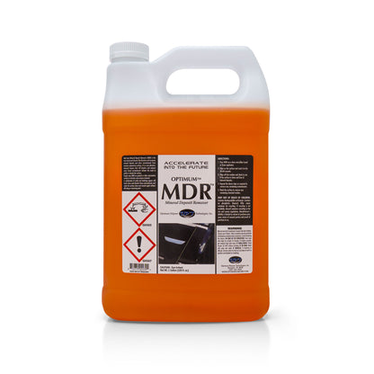 Product photo of a white gallon jug of Optimum MDR Mineral Deposit Remover on a white studio background, filled with bright orange liquid, featuring a white cap, integrated handle, and a prominent black and white label displaying hazard symbols and a car door detail