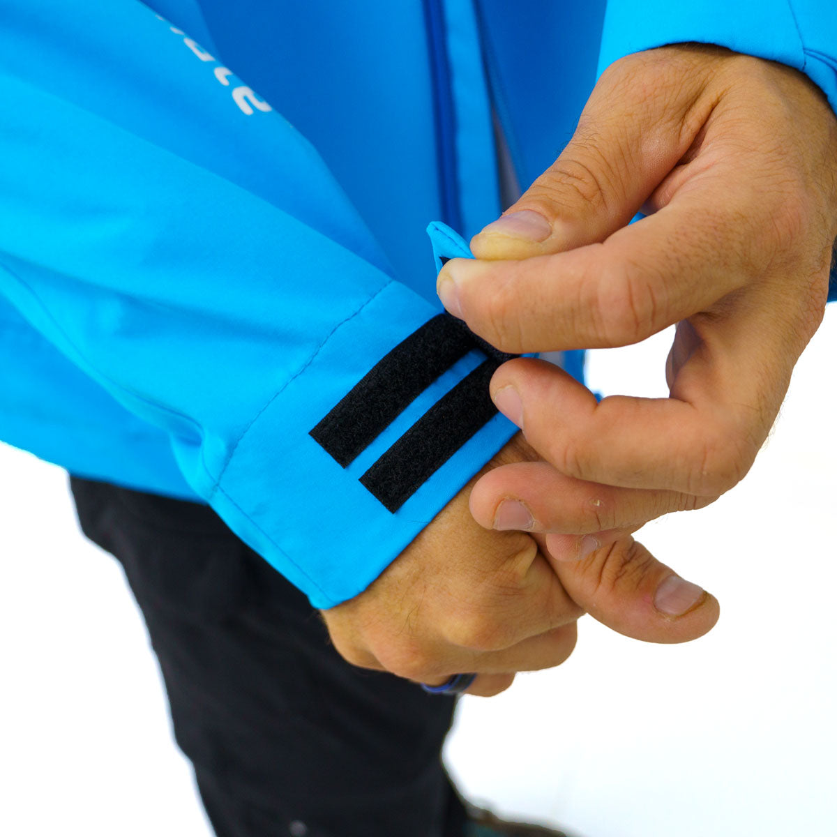 Close-up of hands adjusting the black Velcro cuff straps on a bright blue jacket with white lettering on the sleeve