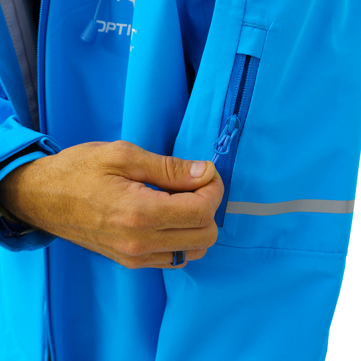 A person's hand zipping a bright blue jacket sleeve pocket, featuring a silver reflective strip and a blue ring