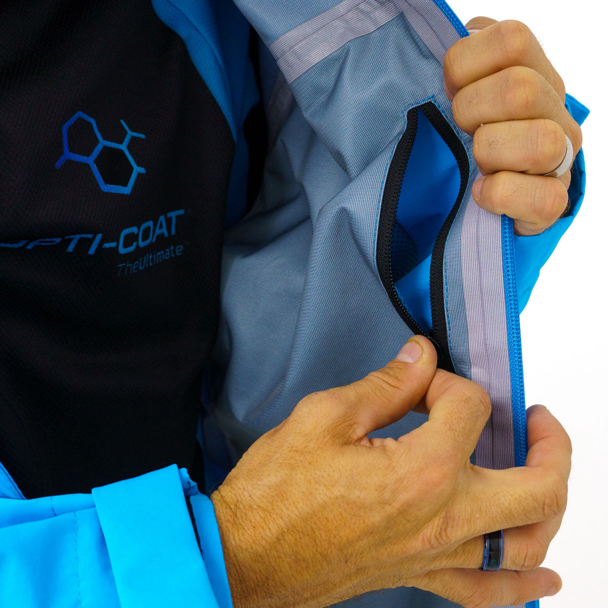 Person's hands demonstrate the interior features of a vibrant blue jacket including a zippered pocket a black shirt with OPTI-COAT The Ultimate branding and a grey lining with reflective detailing