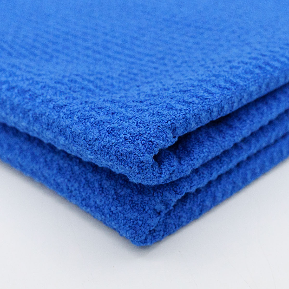 Photograph of vibrant blue stacked towels displaying soft terry cloth texture and three folded layers with subtle ribbed patterns