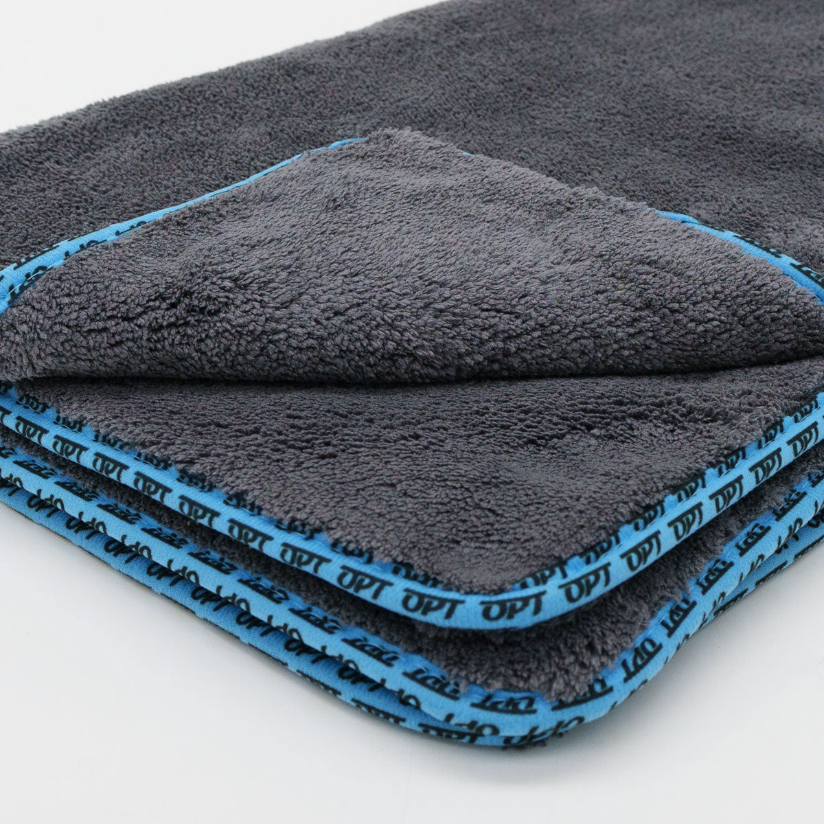 Close-up of a dark grey fluffy microfiber towel folded, featuring a bright blue trim repeatedly printed with the word OPT
