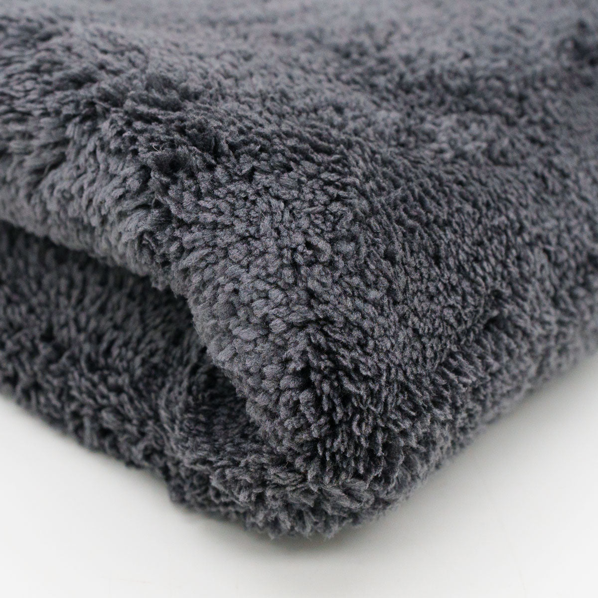 Photograph of a folded dark gray fluffy towel on a white surface highlighting its plush shaggy texture and deep charcoal hue