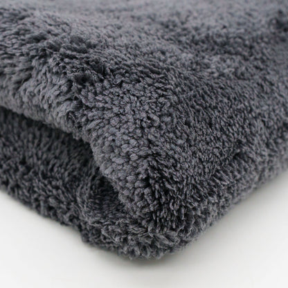 Photograph of a folded dark gray fluffy towel on a white surface highlighting its plush shaggy texture and deep charcoal hue