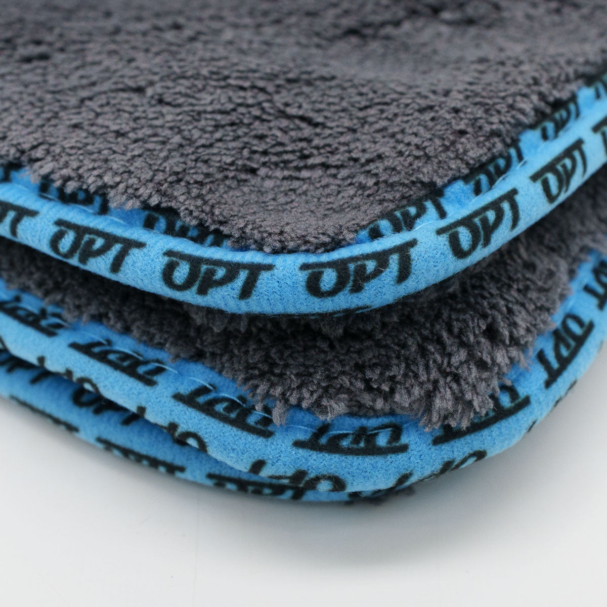 A close-up of a stack of fluffy grey microfiber towels featuring bright blue edges with repeated black OPT logos