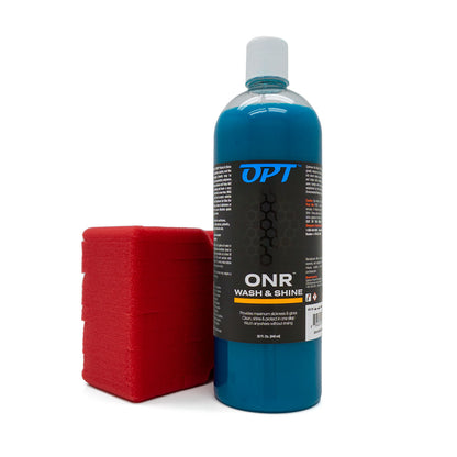 A product photo featuring a clear plastic bottle of OPT ONR Wash & Shine with a white cap and blue liquid, displaying a black OPT logo, positioned next to a bright red rectangular wash sponge on a clean white background