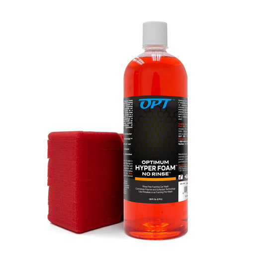 A studio product shot featuring a large clear bottle of vibrant red Optimum Hyper Foam No Rinse car wash liquid with a white cap and black label, alongside a bright red rectangular foam washing sponge on a clean white background