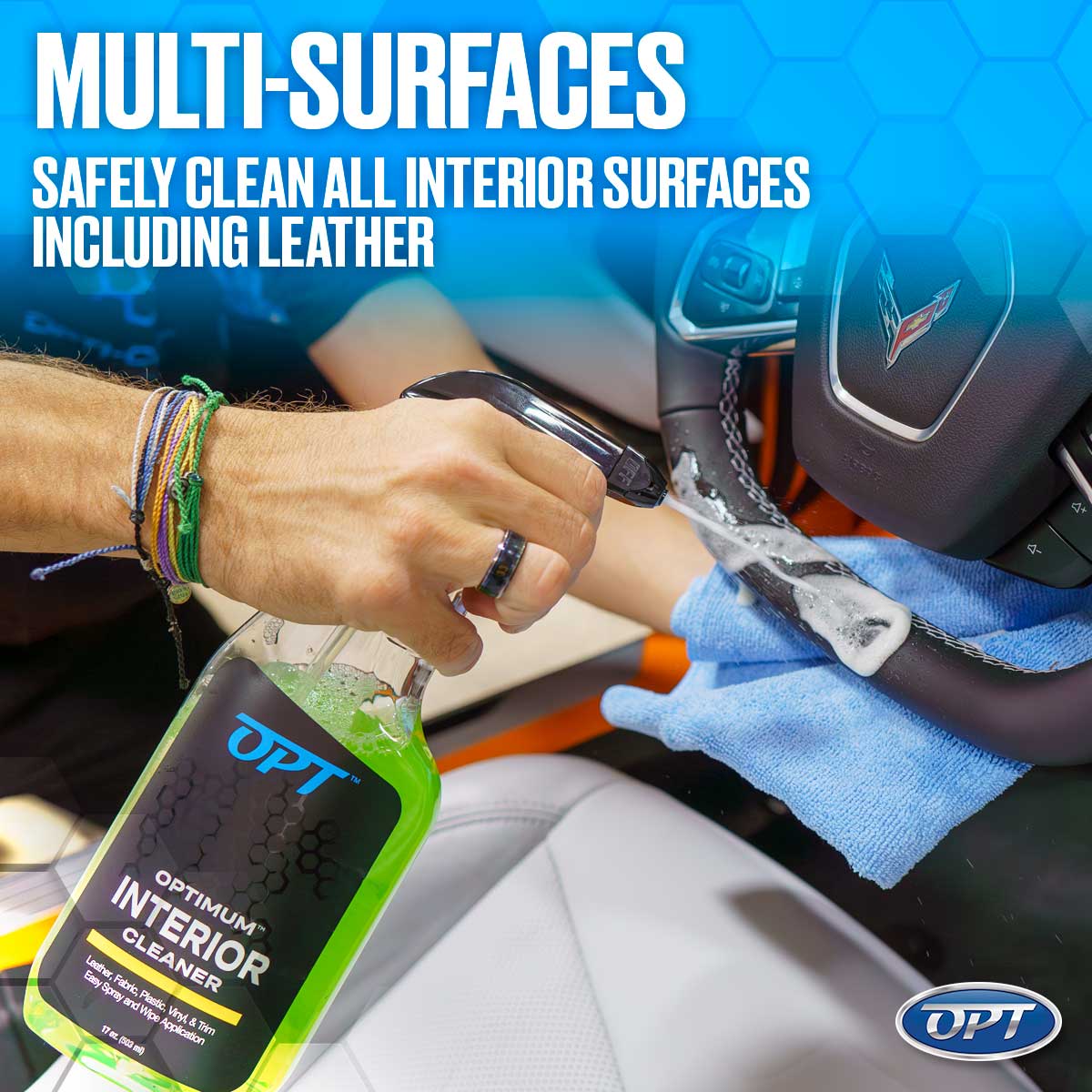 A person's hand, adorned with colorful bracelets, sprays white foam from a green OPT Optimum Interior Cleaner bottle onto a black leather Corvette steering wheel, with a blue microfiber towel ready to clean and white leather seats in the background, promoting safe multi-surface cleaning for car interiors including leather