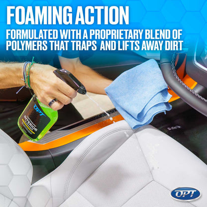 A hand sprays white foam from a bright green Optimum Interior Cleaner bottle onto an orange car interior trim and white perforated leather seat, with a light blue microfiber towel resting nearby