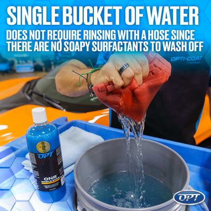 Photograph of a hand wringing a red wash mitt into a grey bucket of blue water, with an OPT ONR Wash & Shine bottle in the foreground and a bright orange car in the background