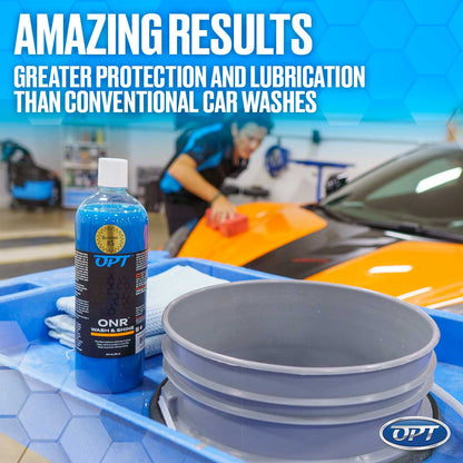 A car detailer in a blue uniform washes an orange and black sports car with a red pad, next to a blue bottle of OPT ONR Wash & Shine and a grey bucket on a blue utility cart in a detailing bay