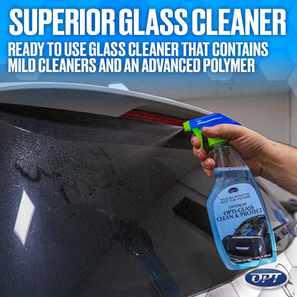 Photograph of a hand spraying blue and green Optimum Opti-Glass Clean & Protect from a bottle onto a dirty car rear window with a red LED brake light visible, promoting Superior Glass Cleaner