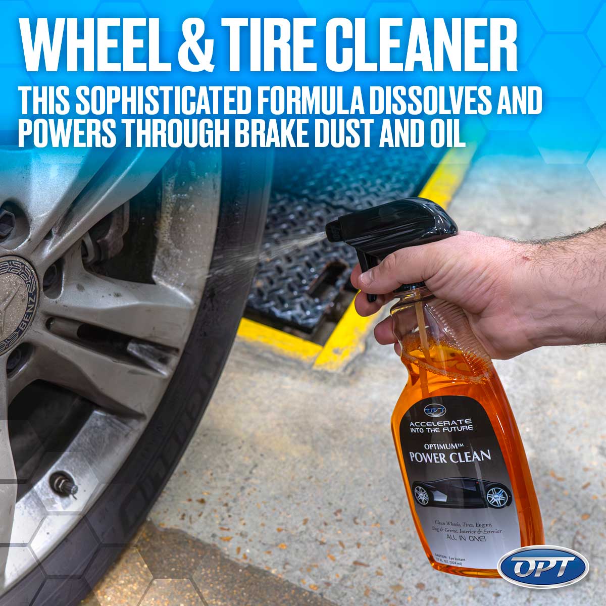 Digital photograph by OPT of a hand spraying orange Optimum Power Clean onto a dirty Mercedes-Benz car wheel with a yellow-striped floor grate and prominent 'WHEEL & TIRE CLEANER' text displayed