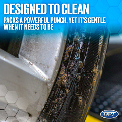 A close-up image of a silver car wheel rim and black tire covered in foamy brown grime and cleaning solution bubbles, featuring the text "DESIGNED TO CLEAN PACKS A POWERFUL PUNCH, YET IT'S GENTLE WHEN IT NEEDS TO BE" on a blue honeycomb background with an OPT logo