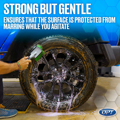 Photograph of a hand using a green-bristled brush to clean a dirty black Jeep wheel with purple foaming soap, featuring a blue vehicle, the text 'STRONG BUT GENTLE', and the OPT logo