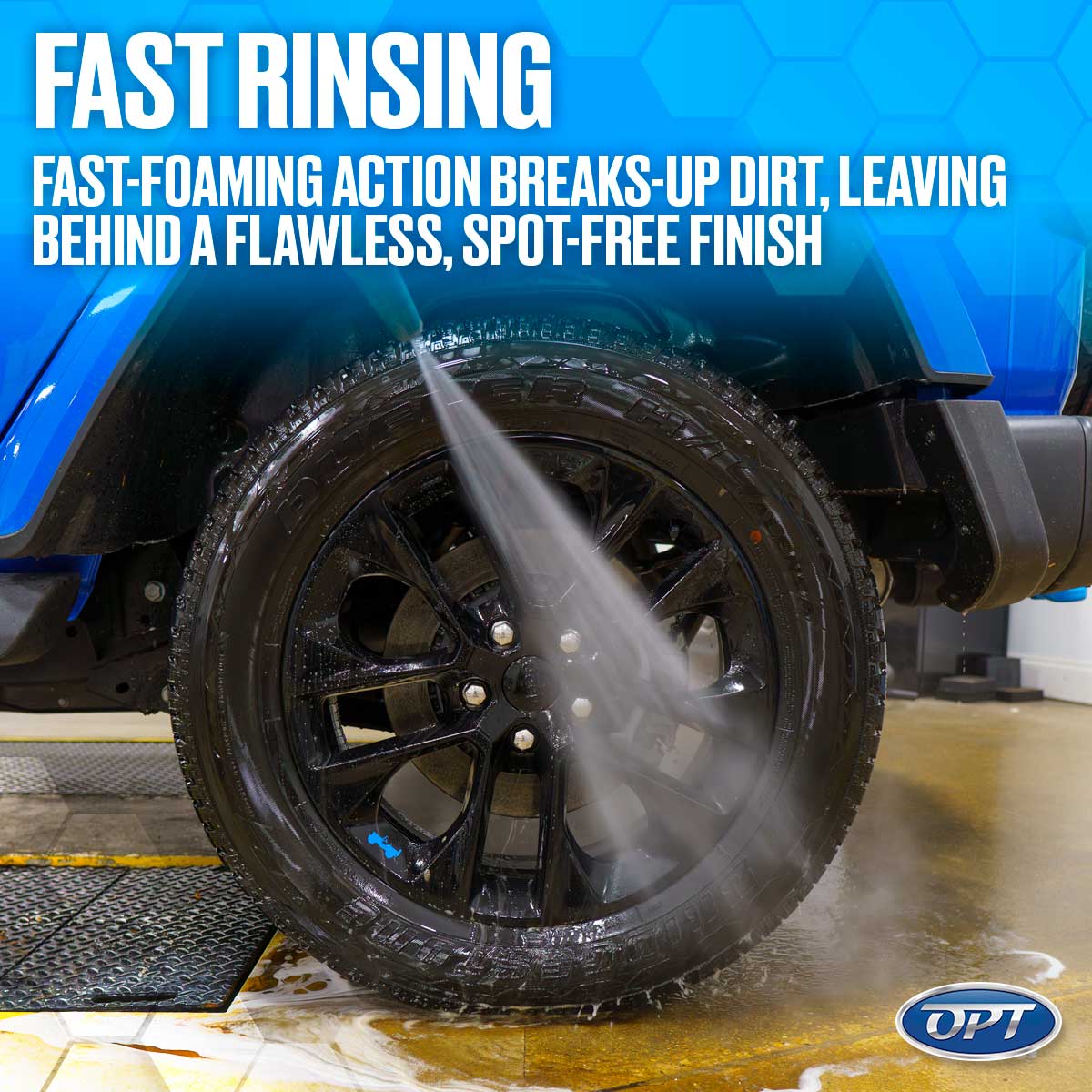 Digital photograph of a blue car's black wheel and tire being rinsed by a high-pressure water jet in a car wash bay with water and suds on the floor and marketing text "FAST RINSING" above