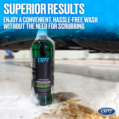 Green Optimum Touchless Decon Wash bottle with overflowing white foam and brown sludge on a tiled garage floor under a dark vehicle, featuring a blue "SUPERIOR RESULTS" banner