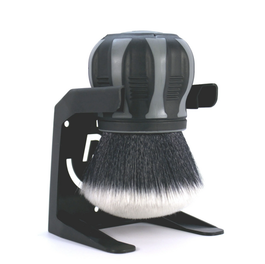 A shaving brush with two-tone black and white bristles and a ribbed black and grey handle sits in a sleek black stand with a decorative cutout