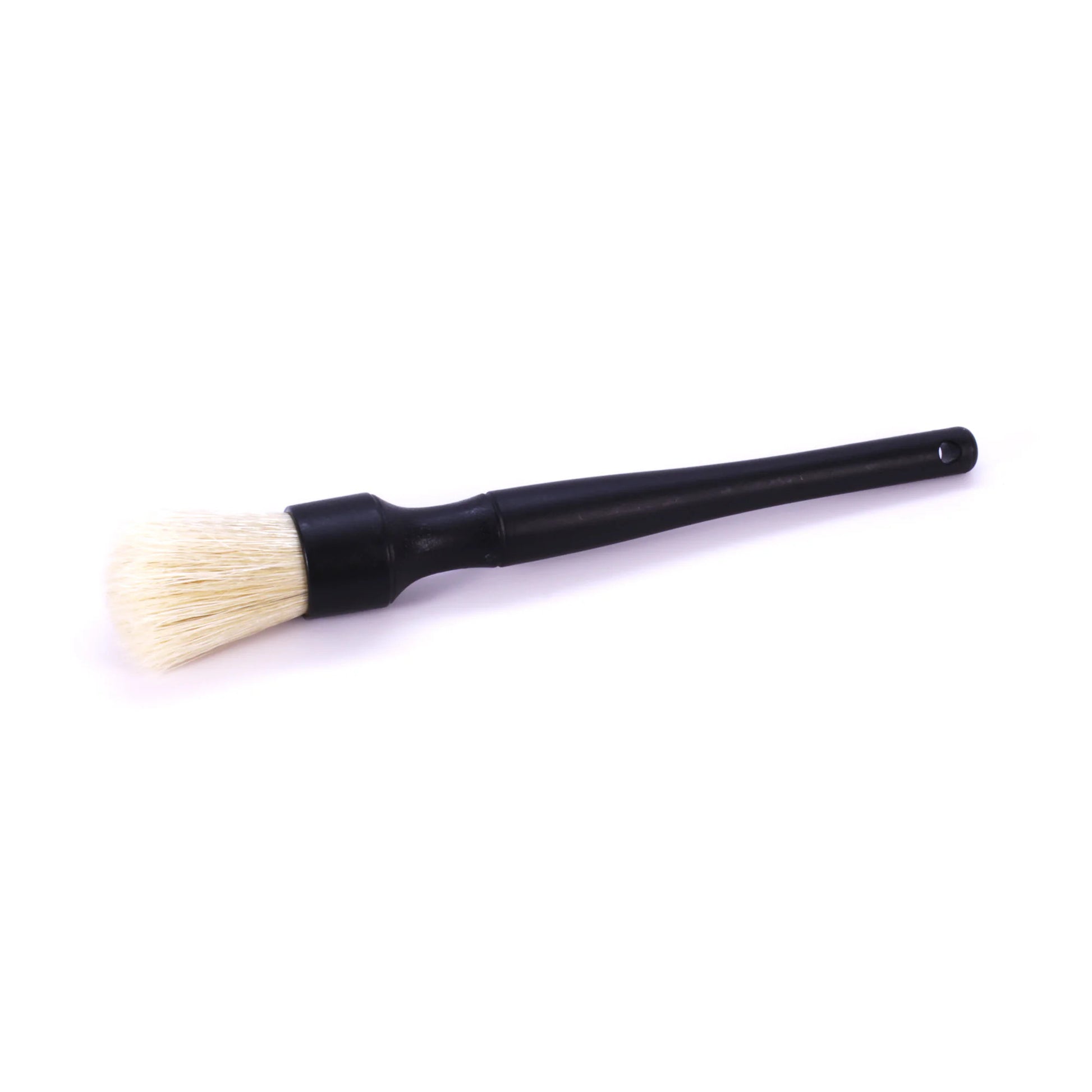 Studio photograph of a black-handled detailing brush featuring soft cream bristles, a silver ferrule, and a small hanging hole at the tapered end