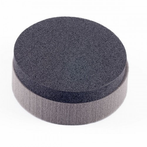 Digital photograph of a round dark gray foam applicator disk with fine pores atop a wider light gray foam base showing subtle texture against a clean white background